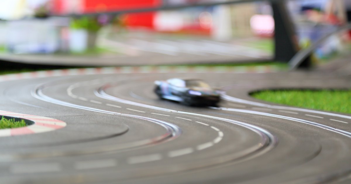 A blurry, up close view of a slot car racing along a track. The track has a groove for the car to ride on.