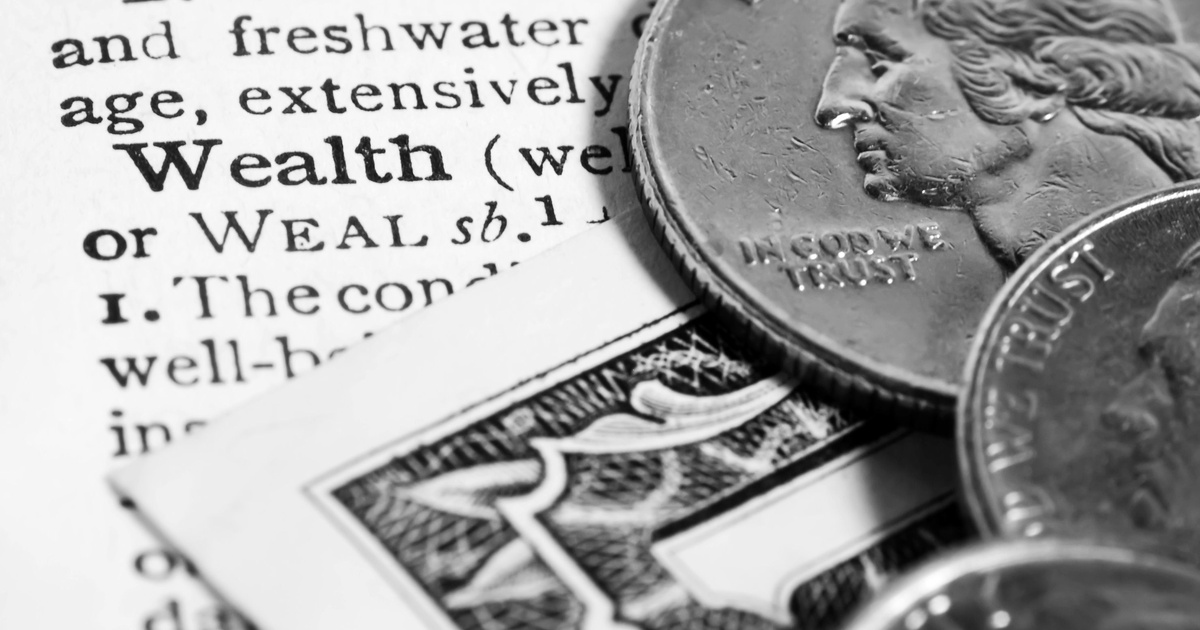 A close-up view of a dictionary entry for the word "wealth," with coins and dollar bills sitting on the page.