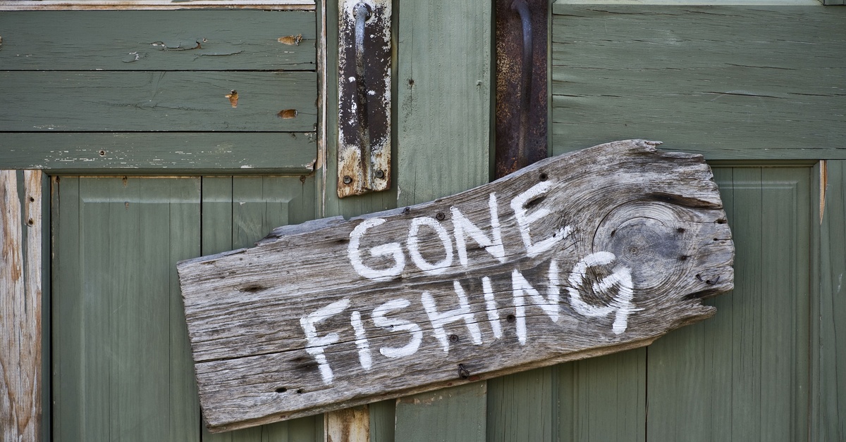 On a weathered olive-green door hangs a gnarled wooden sign that reads "gone fishing" in white paint.