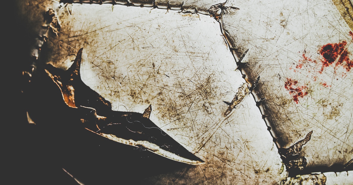 A dirty white football with visible stitches, tears, and gashes in the surface. There is also a red stain.