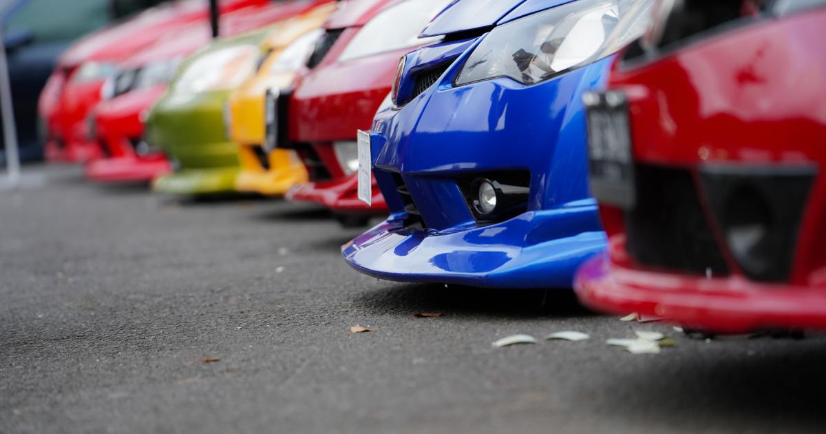 A low-angle side view captures a row of differently colored cars parked bumper-to-bumper in a shaded environment.