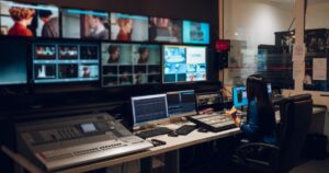 A woman sitting on a leather chair, with multiple screen monitors in front, and a large sound system inside a studio.