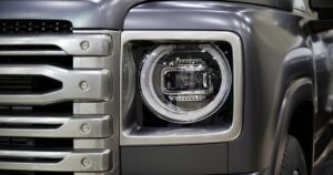 A close-up of the front right headlight of a pickup truck with a silver front grill and a shiny, grey chrome finish.