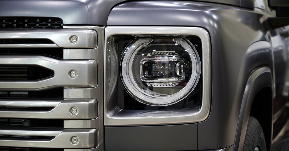 A close-up of the front right headlight of a pickup truck with a silver front grill and a shiny, grey chrome finish.
