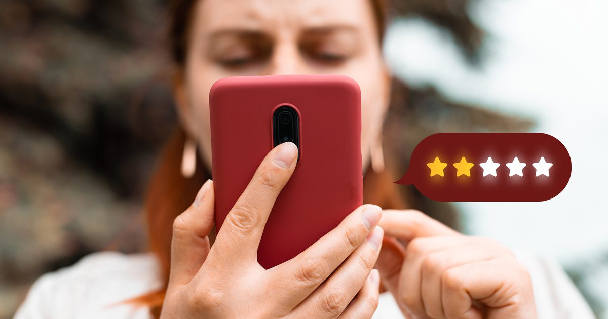 A woman holds a red smartphone close to her face as a two-star rating icon floats beside the screen.