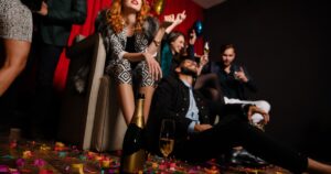 A group of young people sitting on a chair and the floor at a party. There is a scattering of confetti along the floor.