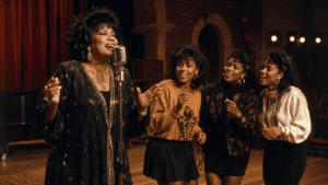 A soul singer rehearsing with three college backup vocalists in a warm late-1980s performance hall